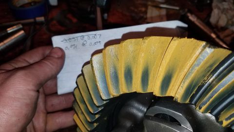 1985 Ford Bronco - A close-up view of a differential gear with yellow marking compound applied to its teeth. A handwritten note with measurements is held near…