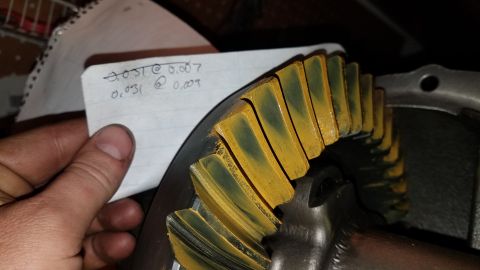 1985 Ford Bronco - A close-up shot shows a hand holding a piece of paper with handwritten notes next to a differential gear. The gear teeth are coated in yell…