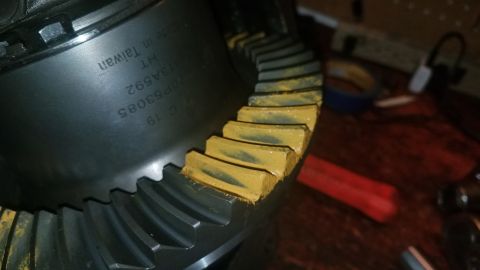 1985 Ford Bronco - A close-up view of a differential ring gear with yellow marking compound on the teeth. The gear has text stamped on its surface, including…