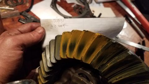 1985 Ford Bronco - A hand holds a piece of paper with handwritten measurements next to a close-up of a differential gear with yellow marking compound on its t…