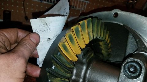 1985 Ford Bronco - A hand holds a piece of paper with handwritten measurements next to a differential gear set. The gear teeth have yellow and green contact m…