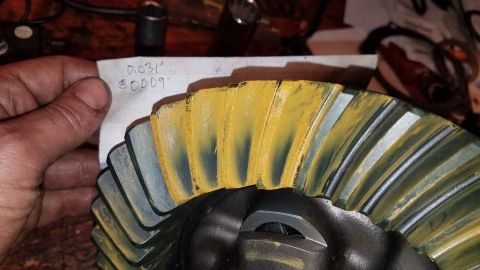 1985 Ford Bronco - A close-up shot shows a hand holding a piece of paper with handwritten measurements next to a differential gear. The gear has yellow markin…