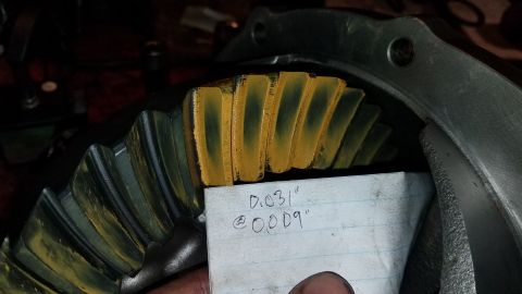 1985 Ford Bronco - A close-up view of a differential gear with yellow marking compound applied to the teeth, indicating contact patterns. A piece of paper wit…