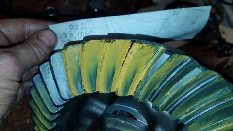 1985 Ford Bronco - A close-up shot shows a hand holding a piece of paper with writing on it above a differential gear. The gear has yellow and blue markings o…