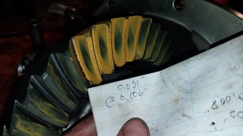 1985 Ford Bronco - A close-up view of a differential gear with yellow marking compound applied to the teeth, indicating contact patterns. A piece of lined pap…