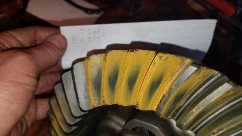 1985 Ford Bronco - A hand holds a piece of paper with handwritten measurements over a differential gear. The gear has wear marks indicated by yellow and dark…
