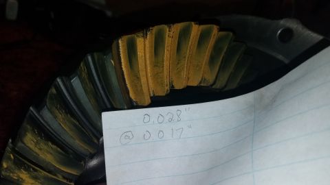 1985 Ford Bronco - A close-up shot of a differential ring gear with yellow marking compound applied to its teeth. A piece of lined paper with handwritten meas…