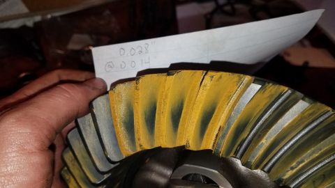 1985 Ford Bronco - A close-up shot shows a hand holding a differential ring gear with yellow and black wear pattern markings on its teeth. A piece of paper wi…