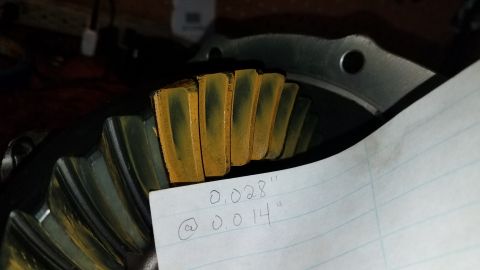 1985 Ford Bronco - A close-up view of a differential gear with yellow marking compound on the teeth. A piece of lined paper with handwritten measurements is p…