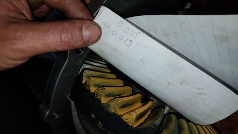 1985 Ford Bronco - A close-up view shows a hand holding a piece of paper with handwritten measurements over a set of gears. The gears appear to be part of a d…