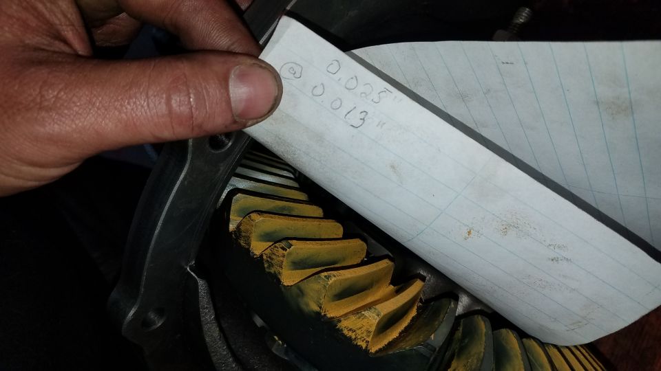 Hand holding paper with measurements 0.025" and 0.013" over yellow gears.