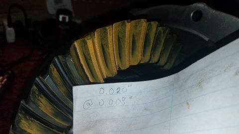 1985 Ford Bronco - A close-up view of a differential gear with yellow marking compound on its teeth. A piece of lined paper with handwritten measurements of "…