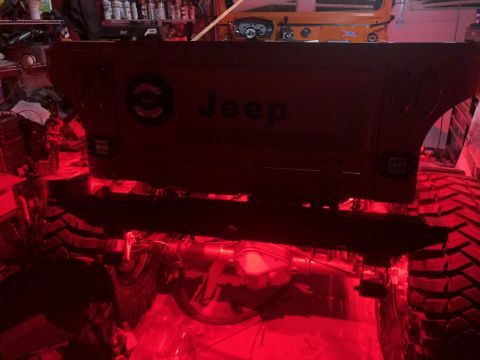 1992 Jeep Wrangler - The rear of a red Jeep Wrangler is illuminated with red underglow lights. The Jeep's tailgate displays the "Jeep" logo and a circular emble…
