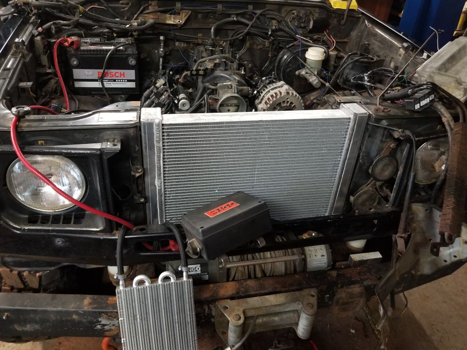 Vehicle engine bay showing a large aftermarket radiator, winch, battery, and engine components