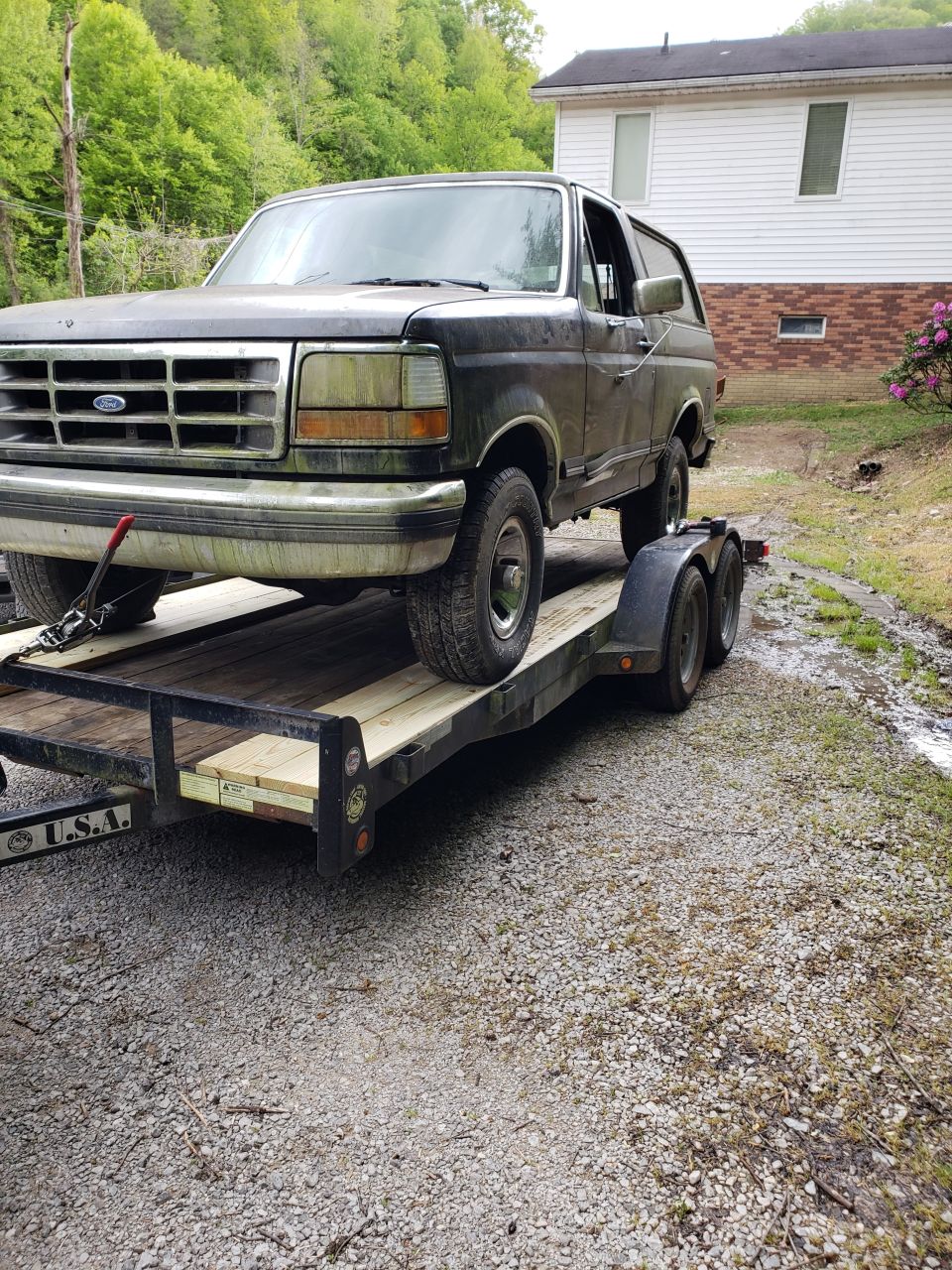 1990 Ford Bronco on a trailer in front of a house.