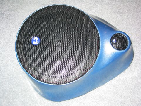 1989 Ford Bronco - Close-up of a single finished custom fiberglass kick panel speaker pod painted metallic blue, with a large black mesh-grilled woofer and a…