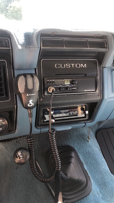 1981 Ford Bronco - The interior of a vehicle shows a dashboard with a CB radio and microphone, a gear shifter, and an air conditioning control panel. The dash…