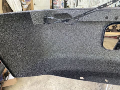 1994 Ford Bronco - Close-up shot of a black, textured aftermarket bumper with a cut-out section. The bumper appears to be made of metal and has several mounti…