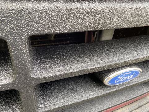 1994 Ford Bronco - A close-up view of a black textured Ford Bronco grille with the blue and silver Ford oval emblem visible.
