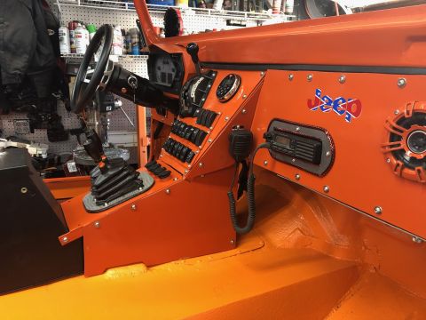 1992 Jeep Wrangler - The interior of an orange Jeep Wrangler shows the dashboard with a steering wheel, gear shifter, multiple switches, a CB radio, and a "Jeep…