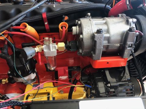 1992 Jeep Wrangler - A close-up view of a modified engine bay featuring a red engine block, an air conditioning compressor mounted on an orange bracket, and an…