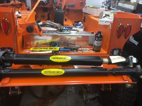 1992 Jeep Wrangler - Two black custom drive shafts with yellow "CUSTOM DRIVE SHAFTS" stickers are mounted on an orange vehicle chassis. A bottle of Castrol Brak…