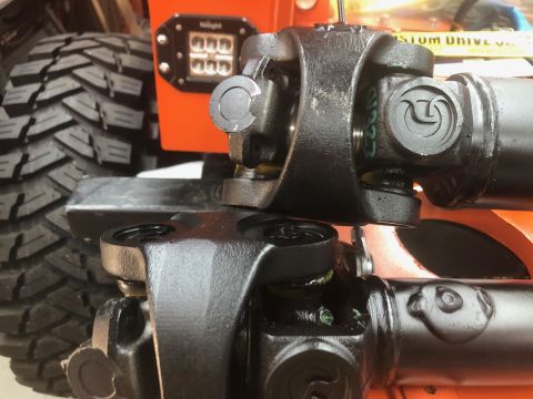 1992 Jeep Wrangler - Close-up view of two black driveshaft universal joints connected to a vehicle's orange frame. A large, knobby tire is visible in the backgr…