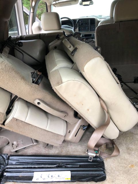 1980 Ford Bronco - The interior of a vehicle shows several removed beige seats piled up on the floor and in the cargo area. A black tool bag with a seatbelt i…