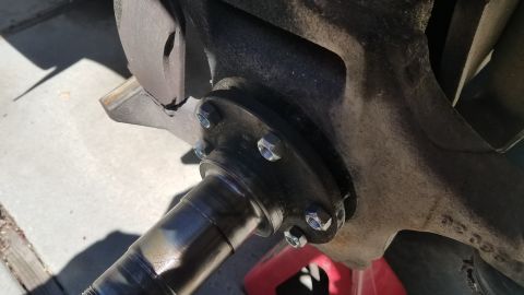 1985 Ford Bronco - A close-up view of a vehicle's wheel hub assembly, showing the spindle and brake rotor attached with bolts. The vehicle is supported by a r…
