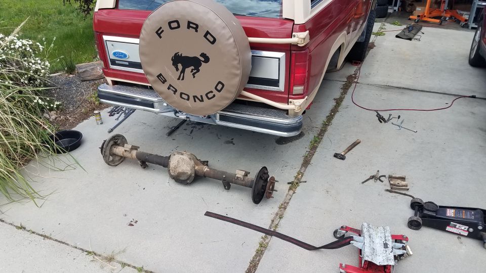 Red Ford Bronco with rear axle removed, tools and jack on concrete.