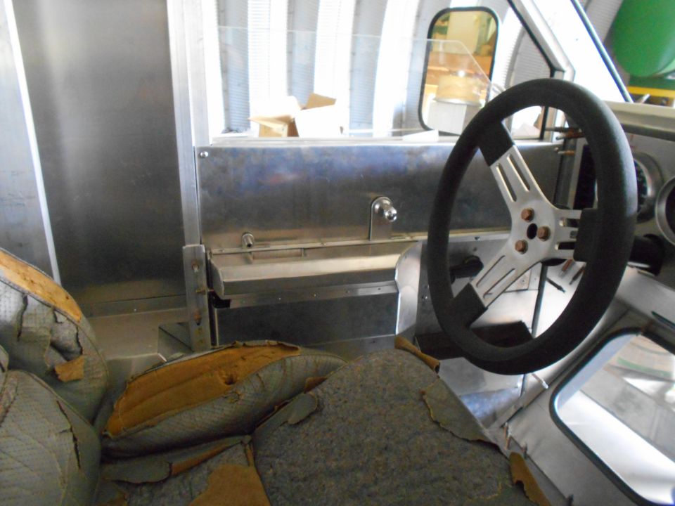 Interior of a vehicle with worn seats and a metal dashboard with a steering wheel.