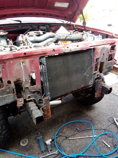 1994 Ford Bronco - The front end of a red vehicle is shown with the hood open, revealing the engine compartment and radiator.