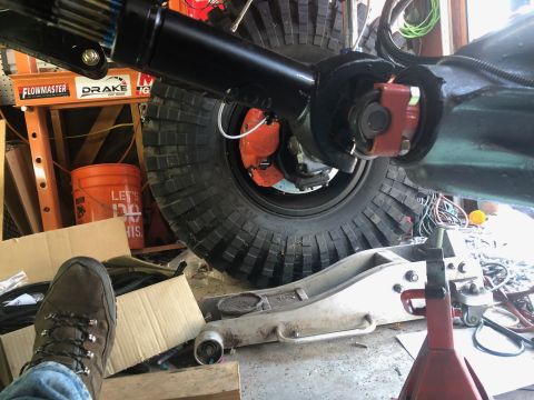 1992 Jeep Wrangler - A close-up view of the rear axle and driveshaft connection on a vehicle, with a large off-road tire and orange brake caliper visible. The v…