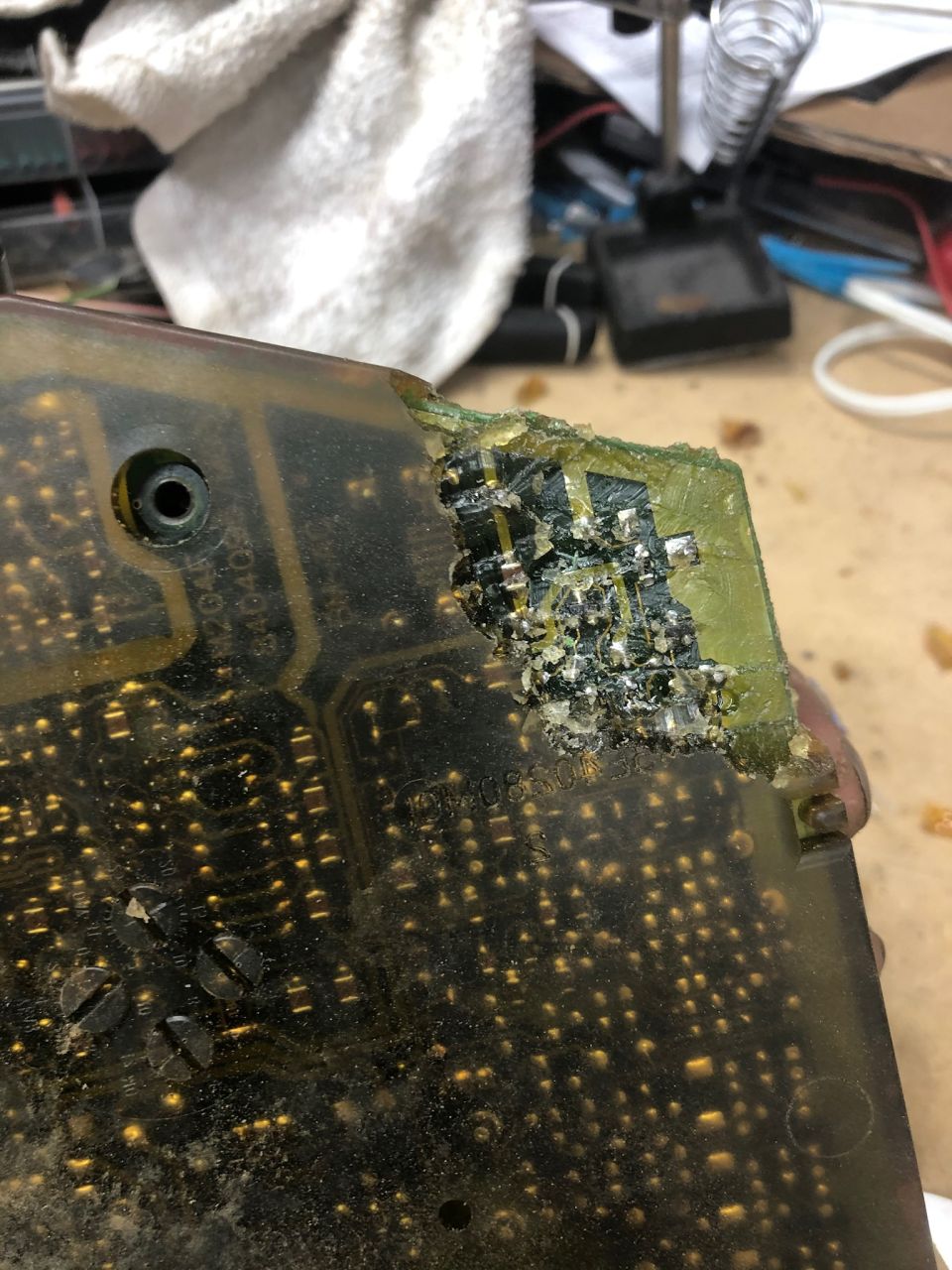 Damaged electronic circuit board with burnt components and corrosion.