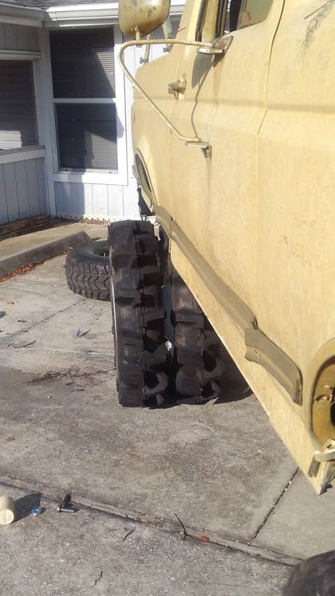 1988 Ford Bronco - A side view of a tan, lifted Ford Bronco with large, aggressive off-road tires. Another tire is visible lying on the ground next to the veh…