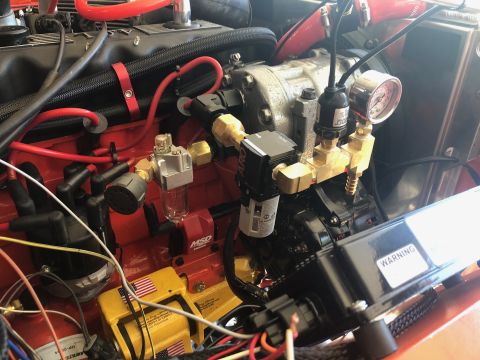1992 Jeep Wrangler - Close-up view of a modified engine bay, featuring a red engine block, various hoses, wiring, a pressure gauge, and an air filter assembly.