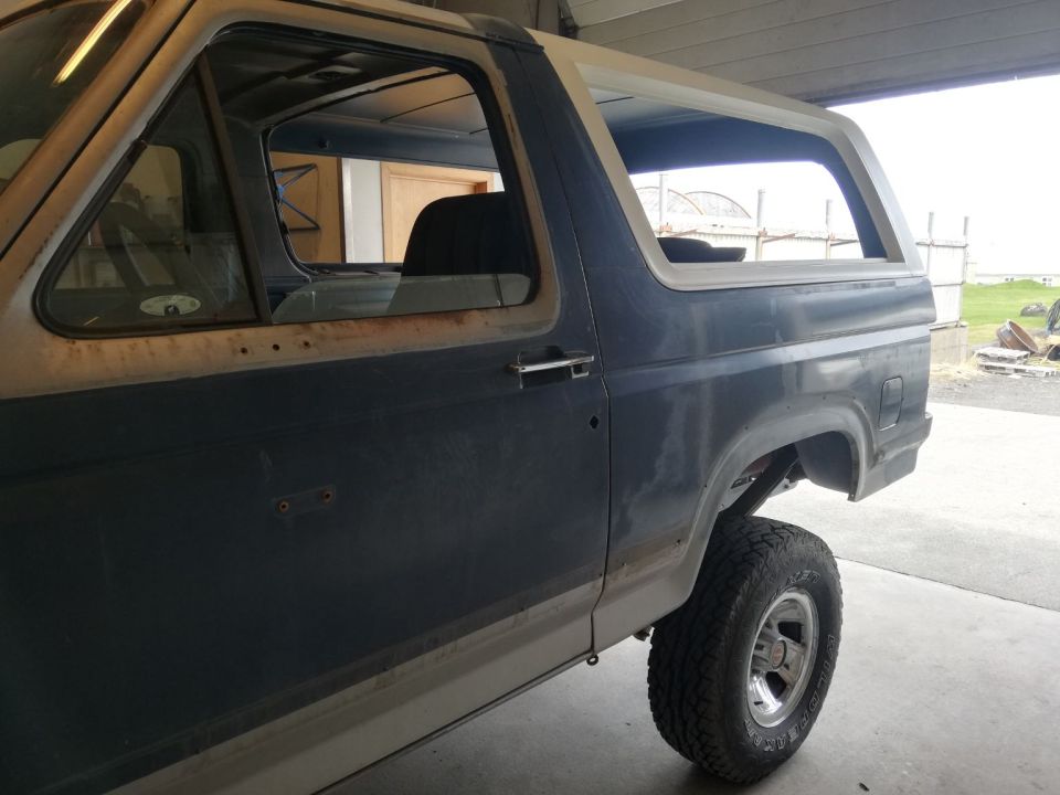 Side view of a dark blue and tan Ford Bronco in a workshop.