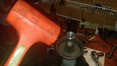 1985 Ford Bronco - A large orange mallet is held over a metal component with a large nut on top, likely part of a vehicle's drivetrain or steering system. The…