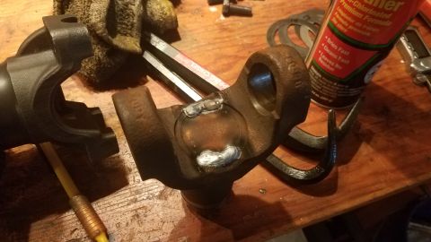 1985 Ford Bronco - A close-up view of a U-joint with fresh welds on a wooden workbench. Several automotive tools and a can of brake cleaner are visible in the…