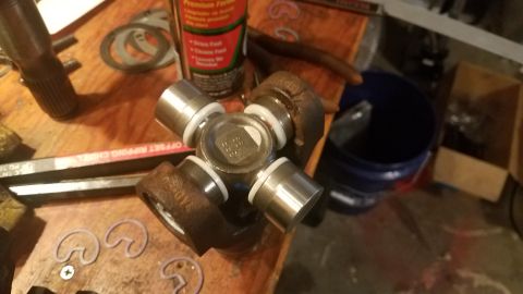 1985 Ford Bronco - A close-up view of a universal joint with white plastic bearing seals and a metal center cap with visible markings. The part rests on a woo…