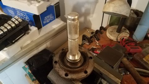 1985 Ford Bronco - A close-up view shows a metal bearing race installer tool being used on a rusty flange with bolt holes. In the background, a blue box with…