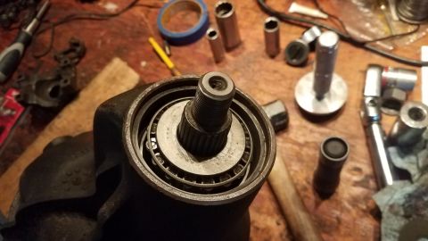 1985 Ford Bronco - A close-up view of a disassembled vehicle part, likely a steering component, showing a bearing assembly with a threaded shaft. Various tool…