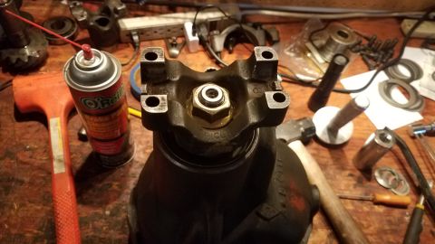 1985 Ford Bronco - A close-up view of a differential housing with a u-joint yoke attached, resting on a workbench with various tools and parts scattered aroun…