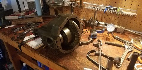 1985 Ford Bronco - A differential housing with internal gears is disassembled on a wooden workbench. Various tools, including a torque wrench, sockets, and a…