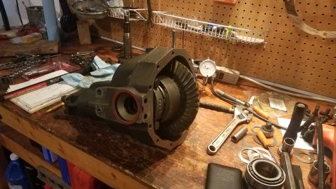 1985 Ford Bronco - A differential housing with gears and a dial indicator are on a workbench surrounded by tools, including wrenches and sockets. The scene ap…