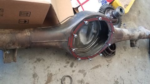 1985 Ford Bronco - A differential housing with a new red gasket and bolts installed is laid out on a concrete floor. A ring gear and pinion gear are visible i…