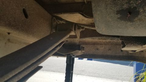 1985 Ford Bronco - The underside of a vehicle shows a leaf spring assembly attached to the frame, supported by a jack. A fuel tank or similar component is vis…