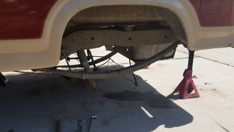 1985 Ford Bronco - The underside of a vehicle, likely a truck or SUV, is shown supported by jack stands. The rear leaf springs and suspension components are v…