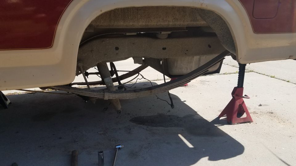 Underside of a vehicle with rear suspension and leaf springs visible, supported by jack stands.