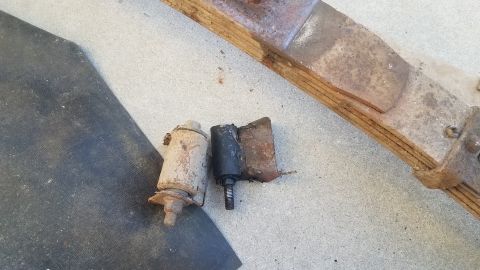 1985 Ford Bronco - Two used suspension bushings and a rusty leaf spring are laid out on a concrete surface next to a black mat.